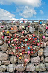 Fototapeta premium Herzform aus Metall befestigt an einem vergitterten Steinstapel mit angeschlossenen Liebesschlössern