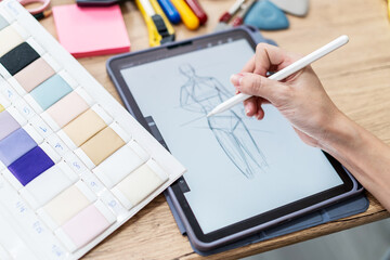 Hand Fashion designer woman draws sketches for a new fashion design, draws on an electronic tablet fashionable clothes. Close up female actively working workspace