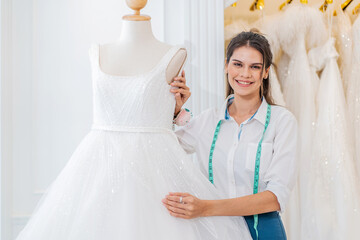 Smiling caucasian woman is bridal shop owner tidying up the wedding dress and looking at camera at...