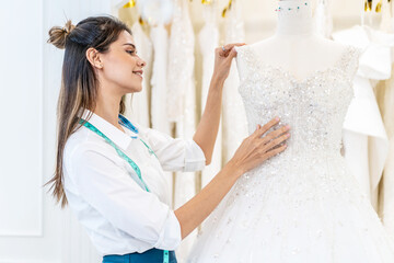 Smiling caucasian woman is bridal shop owner tidying up the wedding dress in office room at wedding...