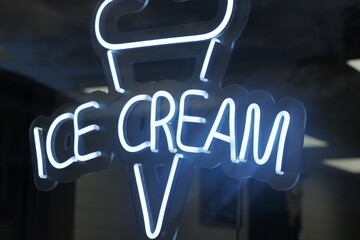 neon ice cream shop sign in window with reflection of cloudy blue sky