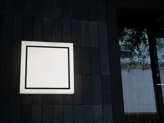 Square frame on mockup of light box signage in front of coffee shop, retail, store near the the entrance glass door. Square light box sign on wooden wall, dark tone.