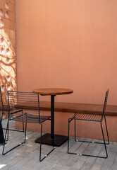 Three empty black wire chairs, long bench seat and round wooden table on gray brick blocks flooring and empty brown terracotta color wall background with copy space, vertical style.