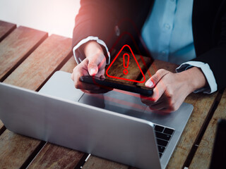 Virus alert. Red triangle, System hacked error sign, malware, attention danger symbol warning showing on smartphone while business person playing online game near laptop computer on desk.