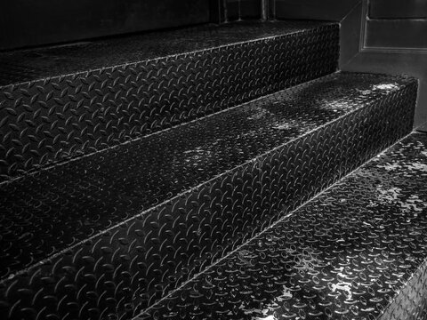 Staircase steps made by metallic checker plate anti-slip texture background. Abstract black metal sheet stair, close-up texture, black and white style.