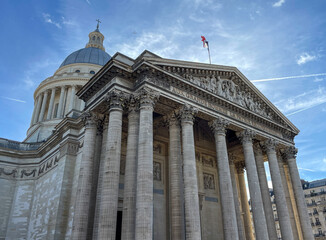 Pantheon building in Paris, France with focus on French flag over blue sky.