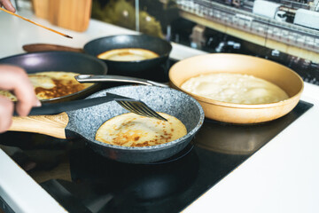 Russia Moscow 14.03.2021 Cooking many big tasty pancakes Lot of pans,oil,pancake dough.Russian traditional national festival winter Maslenitsa holiday week,shrovetide. Man, father cook.Family holiday