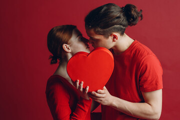 Fototapeta na wymiar Man and woman young couple kissing and hiding behind heart-shaped box.