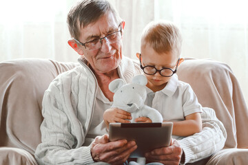 Elderly grandfather and his little grandson use a tablet device together