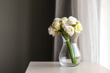 A bouquet of white roses in a glass vase near the gray wall.