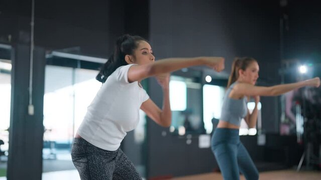 young women friend doing boxing punches body combat crossfit during fitness martial arts workout in training class. Male instructor showing exercise at fitness gym