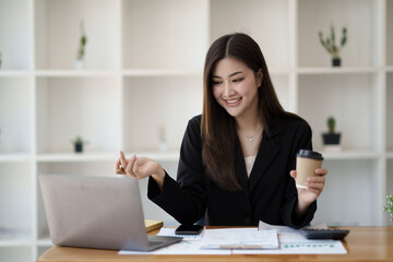 Happy Asian businesswoman working for her project and drinking coffee cup while working, sitting at the office desk.