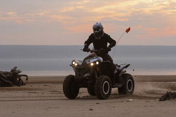 athlete rides a quad bike on the beach at the sunset