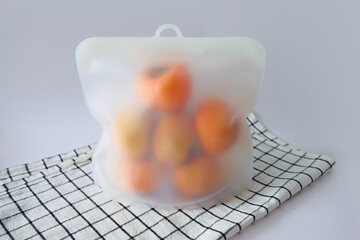 Asian persimmons stored in reusable silicone bag, to keep them fresh; dish cloth with lines sits...