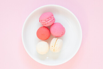 Pink and white macaron cookies served on white plate, pink background, top view