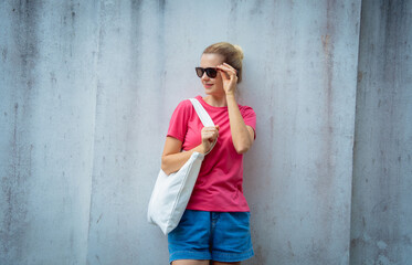 Female model wearing pink blank t-shirt on the background of an gray wall.