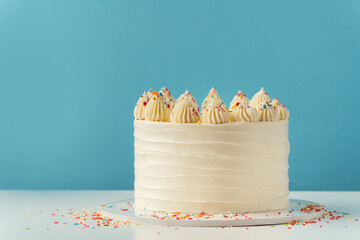 Birthday cake with white cream cheese frosting decorated with multicolored lit candles on a blue...