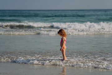 Little girl in swimsuit standing in sea, enjoying holiday.
