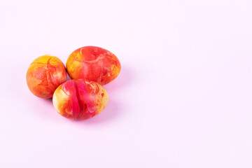 Three painted Easter eggs in red yellow and orange on pink background with a place for text. Happy Easter concept. Greeting card.