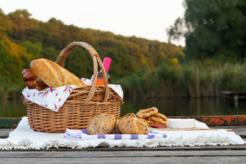 Picnic by the lake with a wicker basket,  food and wine inside, placed on a blanket. Beautiful view
