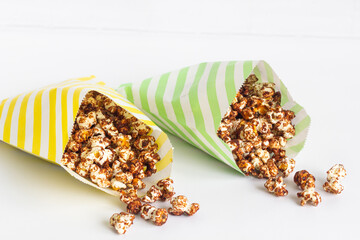 Freshly popped chocolate popcorn in colorful striped paper bag, white background