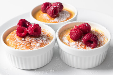 Freshly baked glass dessert in ceramic jars served with fresh raspberries, white background