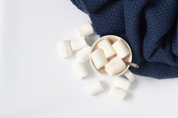 A cup of hot chocolate with soft marshmallow and a cozy blanket on white background, top view.