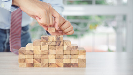 Hand placing wooden block tower stack in pyramid stair step with caution to prevent collapse or...
