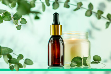 Brown glass dropper bottle with eucalyptus serum or oil on glass shelf on blue background with eucalyptus branches and shadows. Natural cosmetics based on fermented products. Front view, soft focus