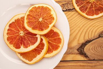 Naklejka na ściany i meble Several dry grapefruit slices with white ceramic plate on wooden table, macro, top view.