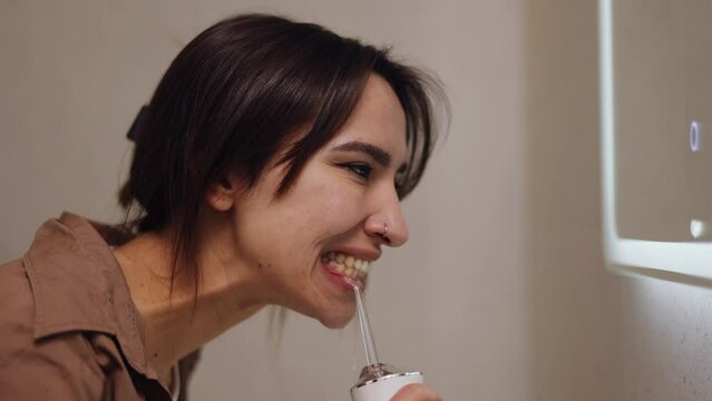 the girl brushes her teeth with an irrigator in front of the mirror