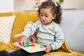Adorable hispanic girl playing maths game sitting on sofa at home