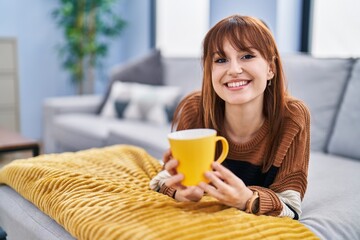 Young woman drinking coffee lying on sofa at home