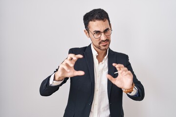 Handsome business hispanic man standing over white background smiling funny doing claw gesture as cat, aggressive and sexy expression