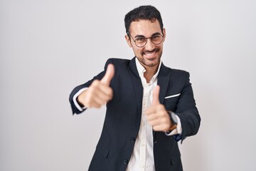 Handsome business hispanic man standing over white background approving doing positive gesture with hand, thumbs up smiling and happy for success. winner gesture.