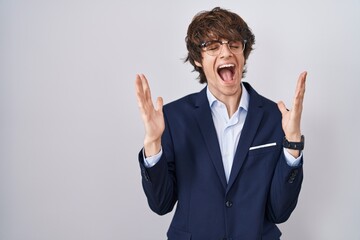 Hispanic business young man wearing glasses celebrating mad and crazy for success with arms raised and closed eyes screaming excited. winner concept