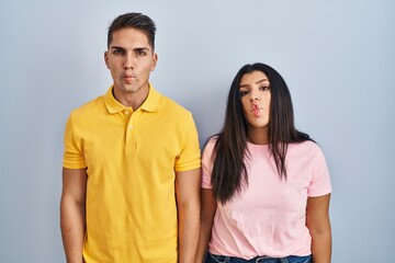 Fototapeta premium Young couple standing over isolated background making fish face with lips, crazy and comical gesture. funny expression.