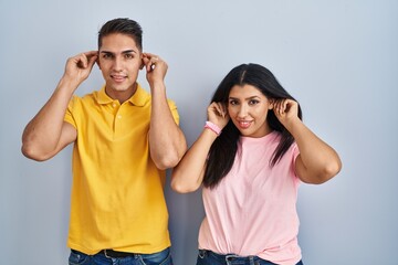 Young couple standing over isolated background smiling pulling ears with fingers, funny gesture. audition problem