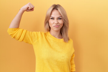 Young caucasian woman wearing yellow sweater strong person showing arm muscle, confident and proud...