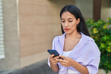 Young beautiful hispanic woman using smartphone with serious expression at street