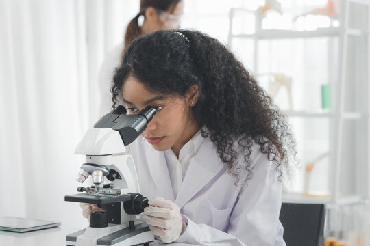 A female scientist is using a microscope to look and doing some experiments or research in the science room