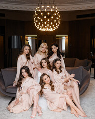 Attractive bride sitting in center near beautiful bridesmaids in beige robes in luxury hotel...