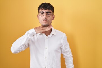 Young hispanic man standing over yellow background cutting throat with hand as knife, threaten aggression with furious violence