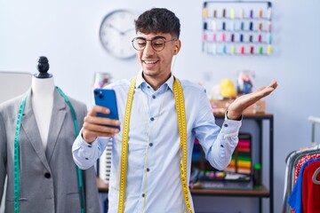 Young hispanic man dressmaker designer using smartphone celebrating achievement with happy smile and winner expression with raised hand