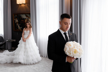 Front view handsome groom with white bouquet of flowers standing in spacious apartment with elegant...