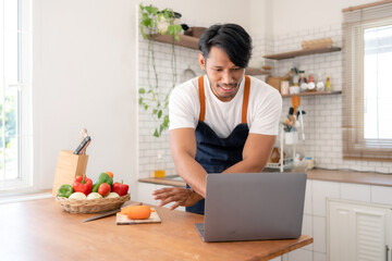 Asian male teacher teaching online cooking is enjoying online cooking in home kitchen using laptop.