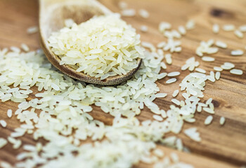 Obraz na płótnie Canvas Close-up view of uncooked white rice in a spoon on wooden background
