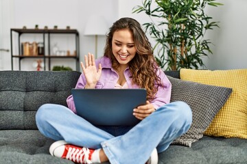 Young beautiful hispanic woman having video call sitting on sofa at home