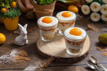 Ei im Glas geschichtet als Dessert zu Ostern auf Untergrund und Hintergrund aus Holz mit Blumen und Deko