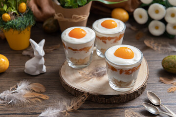 Ei im Glas geschichtet als Dessert zu Ostern auf Untergrund und Hintergrund aus Holz mit Blumen und...
